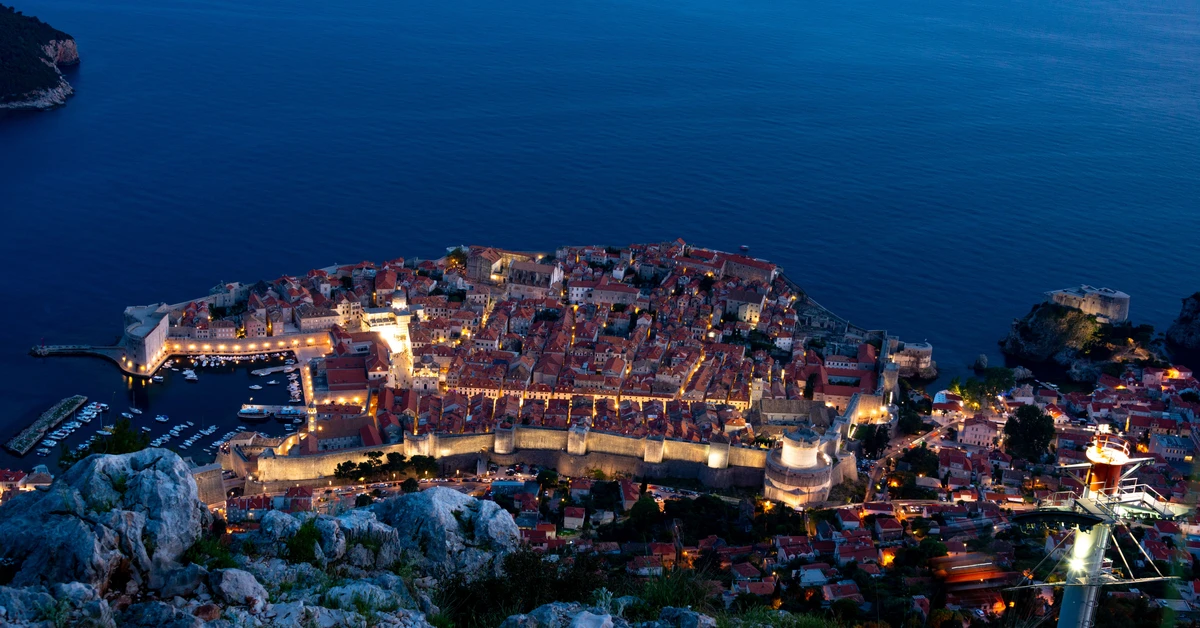 Panoramic twilight view from Mount Srd overlooking the illuminated stone ramparts and red roofs of Dubrovnik Old Town and the Adriatic Sea