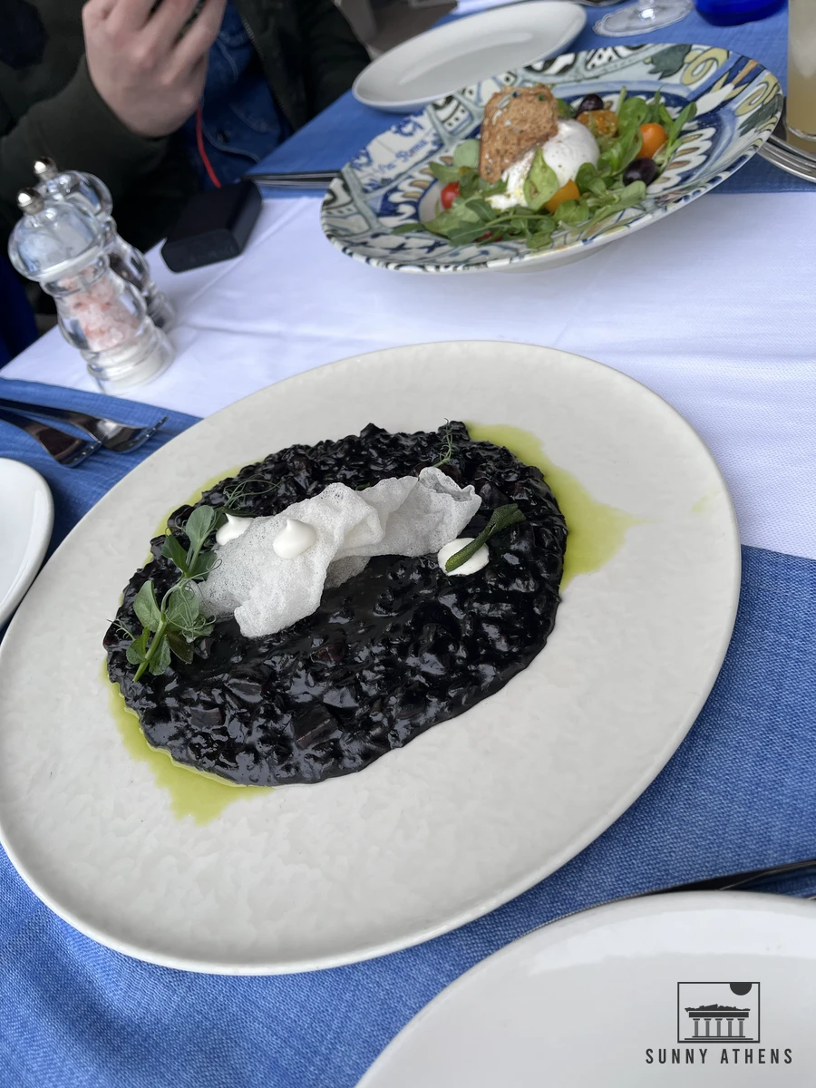 A plate of authentic Dalmatian black cuttlefish ink risotto served with fresh cheese on a seaside restaurant terrace