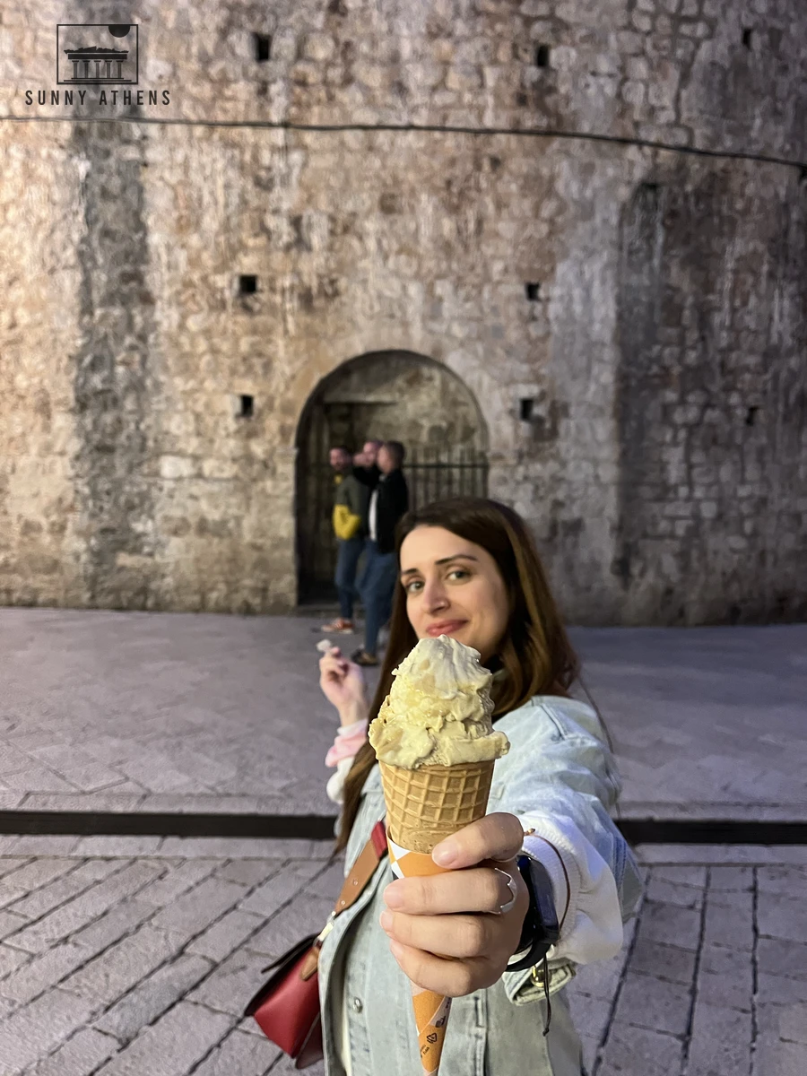 A fresh waffle cone with creamy artisan gelato held against a rustic stone wall in the Old Town
