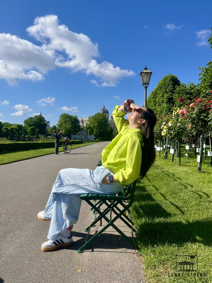 A green park bench surrounded by blooming roses in Vienna's Volksgarten