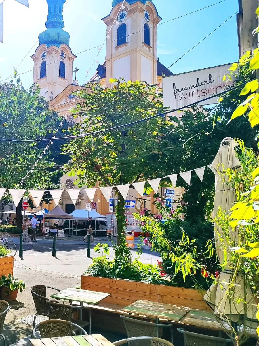 Outdoor wooden dining tables with greenery and white bunting flags outside die freunderlwirtschaft in Vienna's Servitenviertel