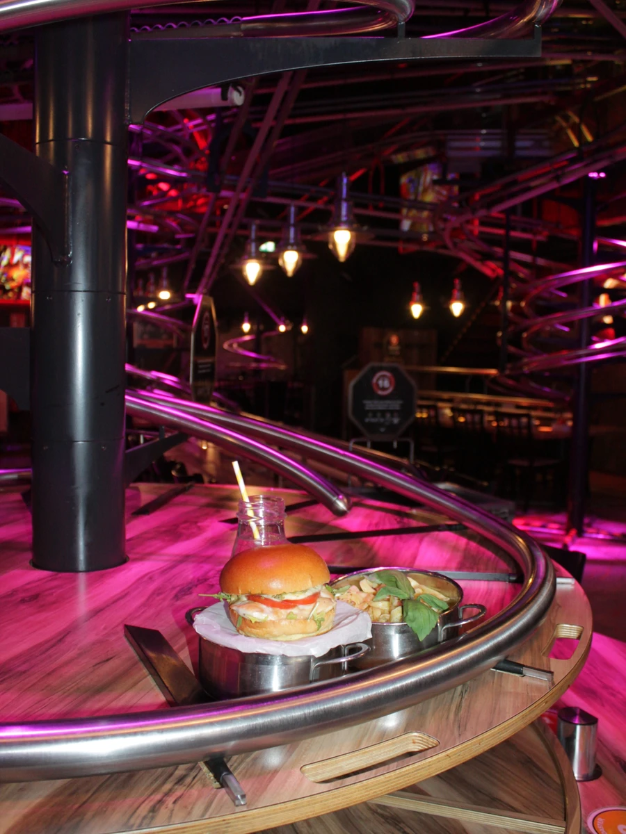 A burger and loaded fries served in metal pots next to the spiraling rail tracks at the Rollercoaster Restaurant in Vienna