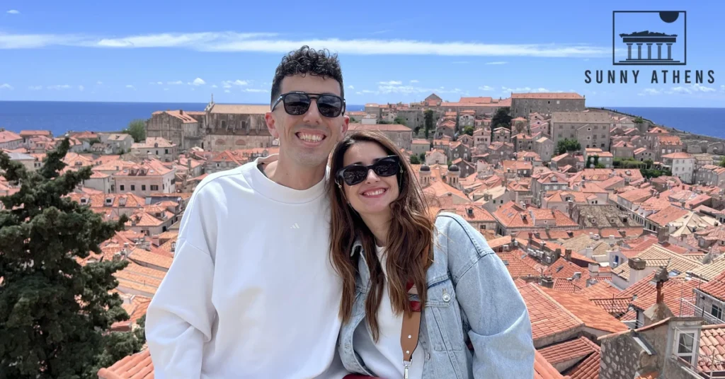 Andreas and Chrysavgi smiling on the elevated stone walkway of the Dubrovnik City Walls with terracotta rooftops in the background