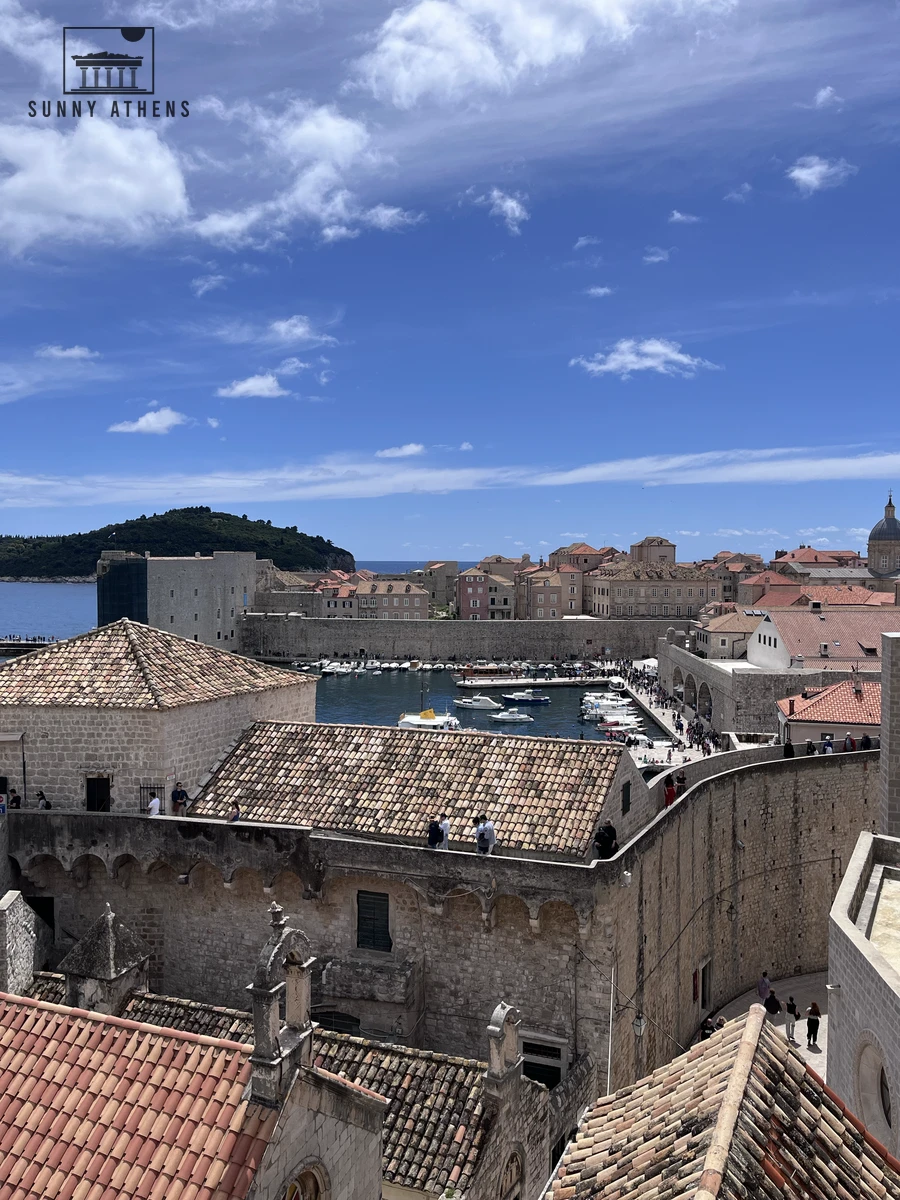Elevated view overlooking the stone fortifications, Old Port harbor, and red tile roofs of Dubrovnik Old Town under a blue sky