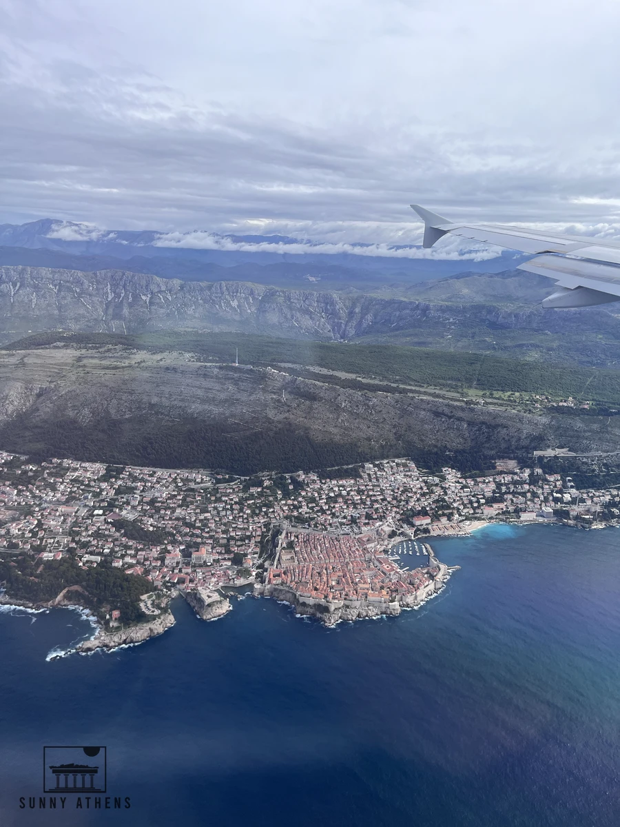 Aerial view from an airplane window looking down at the red-roofed Old Town of Dubrovnik, Mount Srd, and the Adriatic coast