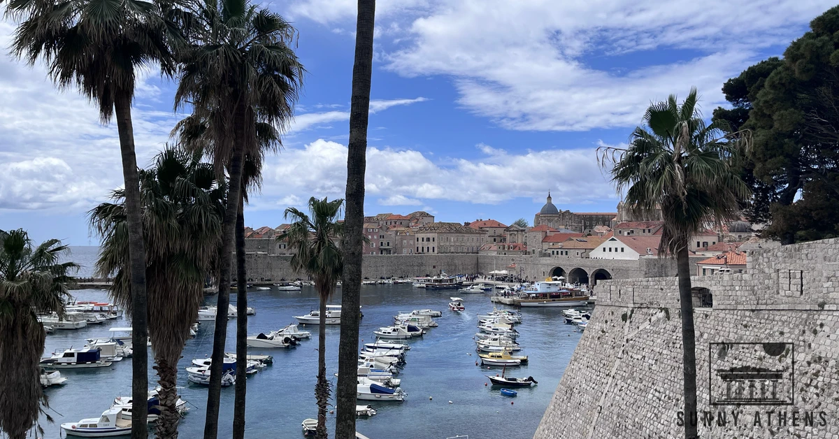 Wide view across the Old Port in Dubrovnik with boats moored in the clear water beneath the fortified stone walls
