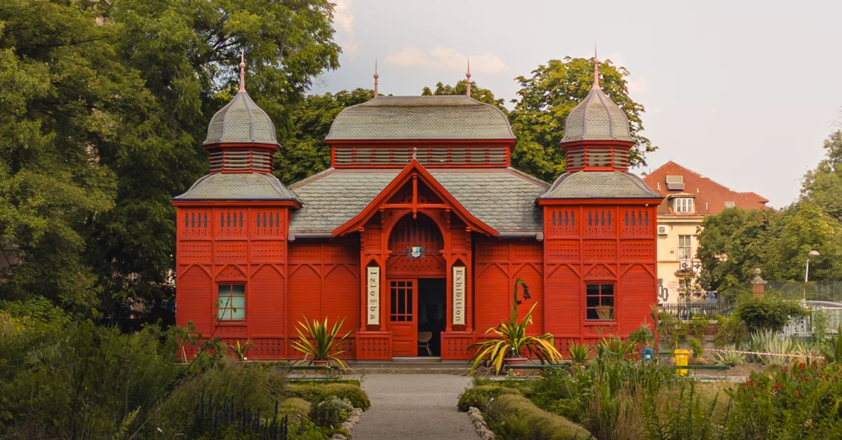 Historic red wooden exhibition pavilion surrounded by green trees and flowerbeds in Zagreb Botanical Garden