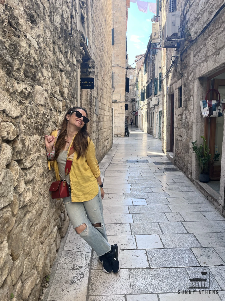 Chrysavgi leaning against a rustic stone wall in a quiet alleyway of Split Old Town