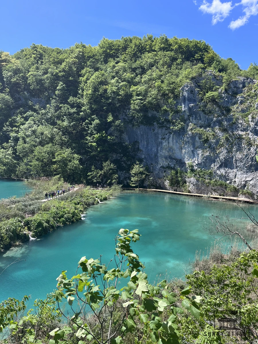 Clear turquoise lake and wooden boardwalk path hugging the limestone cliff in Plitvice Lakes