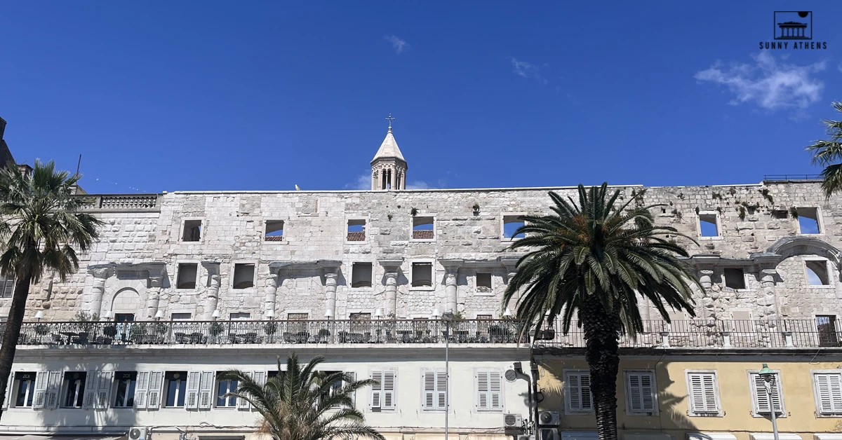Historic stone facade of Diocletian's Palace with Saint Domnius bell tower against a clear blue sky in Split