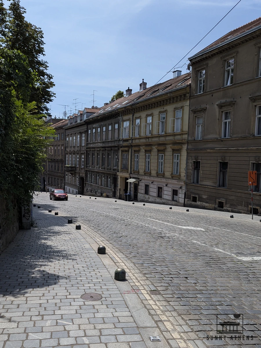 Sunlit paved street lined with 19th-century houses leading up to the Upper Town